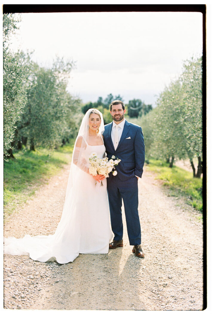 Romantic Film Wedding in Tuscany | Quercia al Poggio Bride and groom pose together on a sunlit olive grove path at Quercia al Poggio, a romantic wedding venue in Tuscany, captured on film.