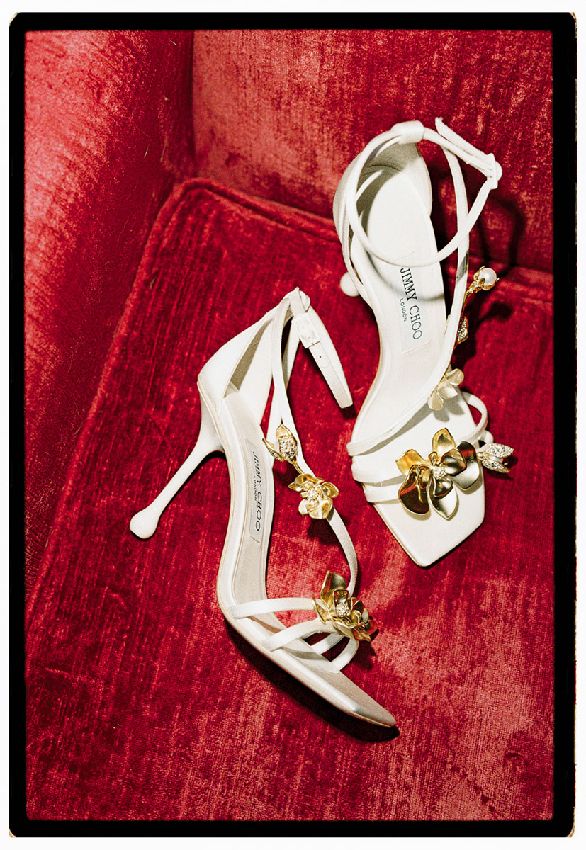 bride-villa-pozzolo-wedding-jimmy-choo-shoes-zea-95-detail-film-photography-01 Jimmy Choo Zea 95 wedding heels with sculpted gold flowers displayed on a red velvet chair at Villa Pozzolo taken on 35mm film.