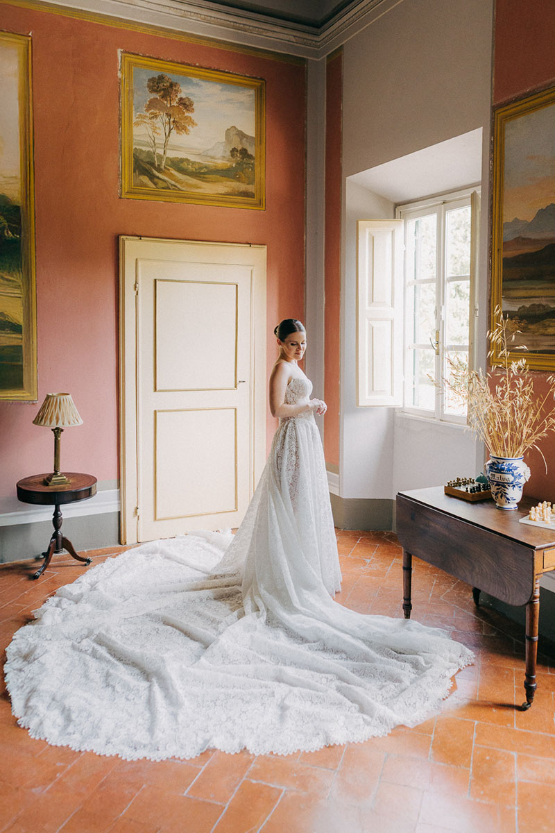 bride-villa-pozzolo-wedding-whole-body-portrait-long-galia-lahav-opera-gown-10 Full body view of the bride standing near a window at Villa Pozzolo in her Galia Lahav Opera wedding dress, bathed in soft natural light.