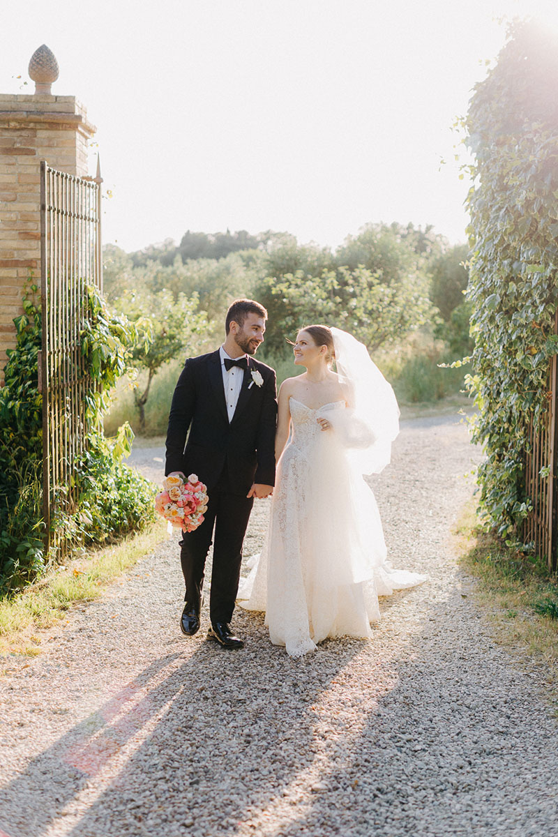 couple-portraits-villa-pozzolo-wedding-couple-walking-bright-light-11 Bride and Groom walk on a gravel path at their wedding at Villa Pozzolo in Montaione, Tuscany. Her Galia Lahav Opera gown shines with the bright light kissing them.