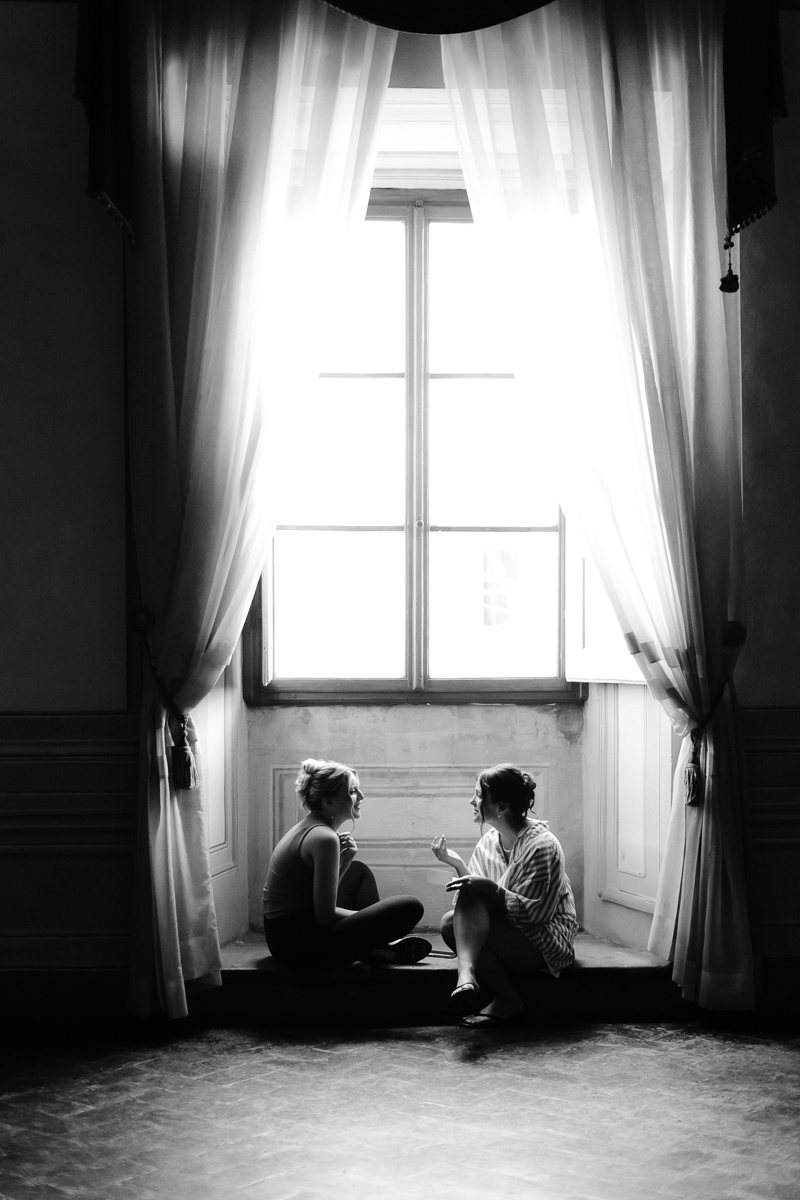 Black and white documentary photo of two women talking by a window during wedding preparations