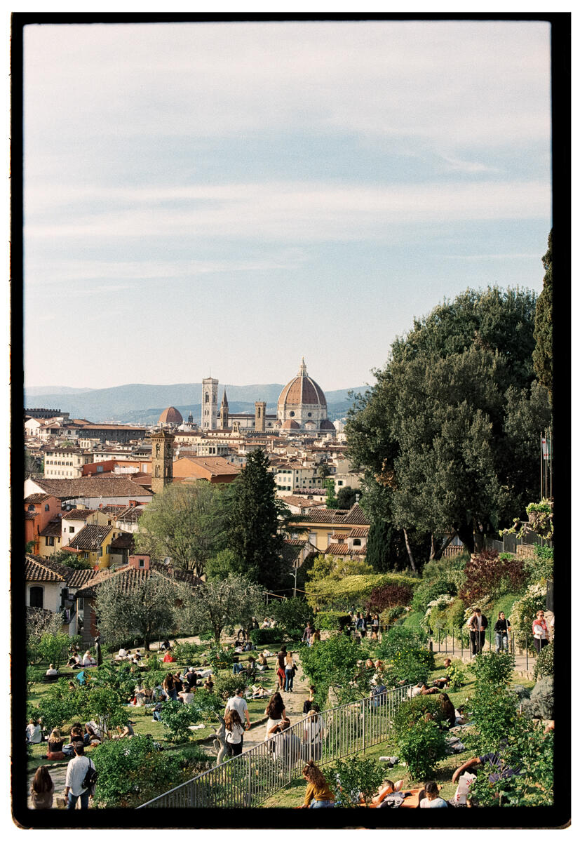 Film photograph of a crowd of people relaxing on the terraced gardens of the Giardino delle Rose in Florence, the dome of the Florence Cathedral and the city skyline visible in the background